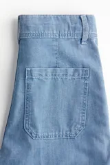 Pantalón de jean de denim rígido, color celeste claro, tiro alto, pierna amplia y corte holgado. Presenta pliegues frontales y traseros, cierre con botón y bolsillos parche en la parte delantera y trasera.