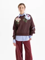 Buzo de corte oversize color marrón chocolate, con cuello redondo y diseño estampado de flores en la parte frontal. Presenta mangas largas con puños ajustados.