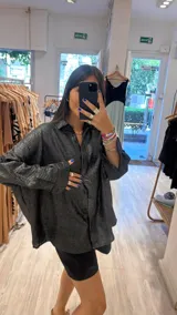 Camisa oversize color verde militar con finas rayas verticales de lurex, cuello camisero y mangas largas con puños anchos.