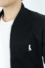 Campera bomber negra de gabardina con cierre frontal, cuello, puños y ruedo acanalados. Tiene bolsillos laterales y logo bordado en el pecho.