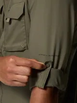 Camisa de manga larga Columbia, color verde militar, con cuello clásico, cierre frontal de botones y dos bolsillos frontales con solapa. Presenta tecnología de protección solar y tejido transpirable de secado rápido.
