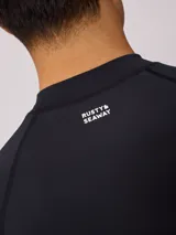 Rashguard de manga larga para hombre, color negro, con cuello redondo y logo de Rusty estampado en blanco en el pecho.