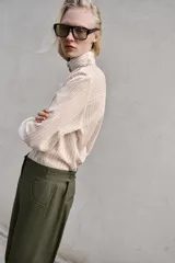 Pantalón de tiro alto en color verde militar, con corte barrel de pernera holgada que se estrecha hacia el tobillo. Presenta trabillas laterales ajustables en la cintura y en el bajo, bolsillos delanteros y cierre frontal con cremallera y botón.