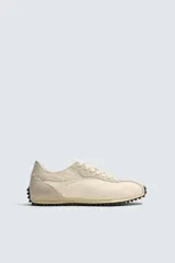 Zapatilla de estilo retro con cordones, confeccionada en tejido técnico y detalles de cuero con acabado serraje. Presenta suela dentada con contraste de color.