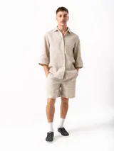 Camisa beige de lino con mangas 3/4, cuello clásico, cierre frontal con botones y bolsillo de parche en el pecho.