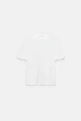 Camiseta blanca de algodón con cuello redondo y manga corta, con detalle de aplicaciones de flores en relieve en los dobladillos de las mangas.
