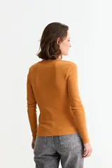 Remera de manga larga, color blanco, con tejido acanalado y escote cuadrado. Presenta un cierre metálico dorado en el centro del escote.