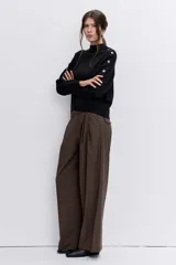 Sweater de punto negro con cuello alto y detalle de ojalillos metálicos a lo largo de las mangas. Presenta un corte holgado con puños y ruedo acanalados.