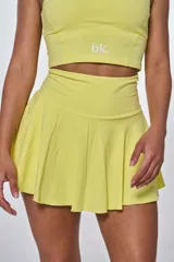 Conjunto deportivo compuesto por un top de escote redondo con logo estampado y una pollera short con diseño plisado, ambos en color amarillo.
