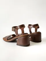 Sandalias de cuero color chocolate, con taco cuadrado de 6 cm, tira ancha en la parte delantera y tira en el tobillo con hebilla metálica ajustable.