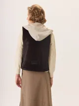 Chaleco con capucha, presenta una espalda de pelo sintético en color marrón oscuro con etiqueta de cuero negra y una capucha de tela tipo denim azul. Diseño original con mezcla de texturas.