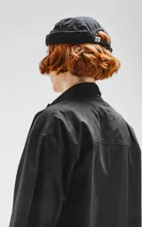 Camisa de manga corta color negro, confeccionada en popelín de algodón, con silueta oversize y dos bolsillos frontales, uno con solapa y otro con ojal y botón.