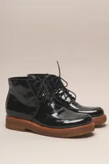 Bota acordonada de cuero vacuno con acabado charol brillante. Presenta una suela de goma tipo crepe en tono natural y costuras reforzadas en la puntera.