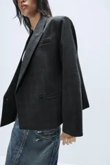 Blazer corto de corte oversize con estampado de cuadros, cuello con solapa de muesca, manga larga y cierre frontal cruzado con un botón. Cuenta con bolsillos decorativos de vivo en el frente y forro interior.