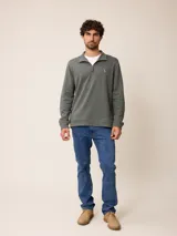 Buzo de polar color verde oscuro, con cuello polo y cierre frontal parcial. Presenta un pequeño bordado en el pecho y puños ajustados.