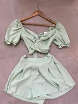 Conjunto de dos piezas color mostaza, compuesto por un top corto de mangas abullonadas con detalle de nudo en el frente y un short de tiro medio con pinzas.