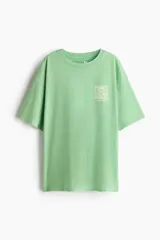 Remera oversized verde de punto de algodón, con hombros caídos, cuello redondo acanalado y estampa pequeña en el pecho con la frase 'Peace Love & Music Woodstock'.