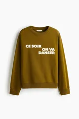 Buzo oversized de color verde militar, con cuello redondo y diseño de texto estampado en el frente. Presenta mangas largas con hombros caídos y terminaciones en ribete acanalado.