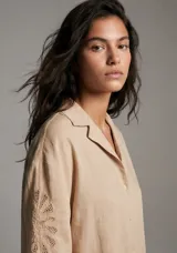 Camisa negra de manga corta con cuello tipo solapa y botones frontales. Presenta bordados sutiles en tono negro en las mangas y en la parte inferior delantera.