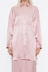 Camisa oversize de satén color rosa, con cuello camisero, manga larga con abertura en puño, cierre frontal con botones y bolsillos en el pecho.