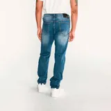 Jeans de hombre, corte slim, color azul claro desgastado (light stone). Presenta cierre de cremallera y botón con logo CAT, diseño de cinco bolsillos y costuras en tono naranja.