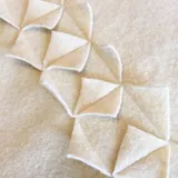 Manta de lana afieltrada color crema, con terminaciones decorativas de figuras geométricas.