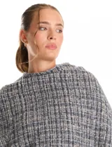 Ruana de tejido tipo tweed en tonos azul y gris con destellos de lurex. Presenta un diseño abierto con terminaciones desmechadas y flecos en todo el borde inferior.