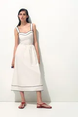 Vestido midi de algodón color blanco, con escote corazón, breteles anchos y espalda con punto smock. Presenta cuerpo entallado, costura fruncida en la cintura y pollera con vuelo, con ribetes negros en contraste en el escote y el bajo.