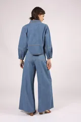 Camisa de denim celeste, de corte cropped, con cuello camisero, mangas 3/4 abullonadas y cierre frontal con botones.