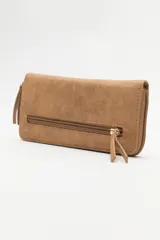 Billetera de formato rectangular con cierre perimetral, confeccionada en material símil cuero de textura suave. Presenta un aplique metálico circular con logo grabado en el frente y tirador de cierre en el mismo material.