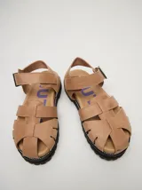 Sandalias tipo romanas de cuero vacuno color beige, con diseño de tiras entrelazadas, hebilla metálica lateral y plataforma de goma dentada.