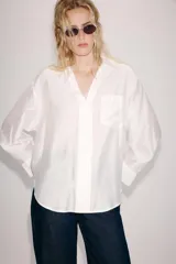 Camisa amplia de cuello solapa con escote en pico y manga larga, en tejido satinado de color bordó. Cuenta con un bolsillo de plastrón en el frente y un diseño holgado.