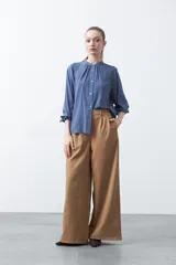 Camisa de color celeste claro con silueta relajada y mangas largas. Presenta un cuello redondo con pequeña abertura frontal y botones, además de un delicado trabajo de tablas en los hombros que aporta textura al diseño.