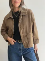 Chaqueta de corte recto color camel, con cierre frontal de cremallera, cuello camisero y puños en tejido de pana a tono. Presenta bolsillos frontales tipo parche y diseño estructurado.