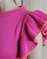 Musculosa de tejido de punto color fucsia con detalles de costuras en color naranja en el cuello, ruedo y volados de las mangas.