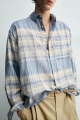 Camisa de corte relajado confeccionada en tejido ligero de algodón, con diseño de cuadros en tonos azules y beige. Presenta cuello solapa, cierre frontal de botones, manga larga con puño abotonado y un bolsillo en el pecho.