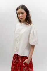 Camisa de popelina de algodón con cuello mao, botones frontales agrupados en pares y mangas cortas abullonadas tipo balloon. Cuenta con un diseño estampado de patrón geométrico y floral sobre fondo negro.