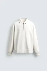 Sudadera polo color blanco roto, de corte regular fit, confeccionada en tejido técnico interlock de algodón elástico. Cuenta con cuello solapa, cierre frontal de cremallera, manga larga y acabados en rib.