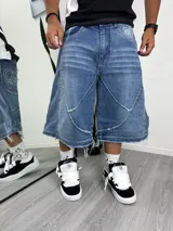 Pantalón de jean ancho, tiro bajo, color azul medio. Presenta paneles superpuestos con costuras expuestas y bordados en blanco en los bolsillos traseros.