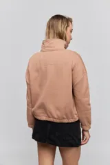 Buzo de calce relajado color tostado, con cuello alto y detalle de cordones entrelazados con ojales metálicos en el frente. Posee bolsillos laterales ocultos y puños y ruedo elastizados.