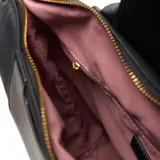 Mochila negra de material símil cuero (PU) con herrajes dorados. Presenta un asa corta superior, correas traseras regulables y un bolsillo frontal con solapa que se cierra con un broche metálico. En el centro de la solapa lleva un logo metálico con las letras "XL".