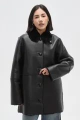 Tapado largo de eco-cuero negro con interior y cuello de piel sintética, cierre frontal con botones y diseño holgado.