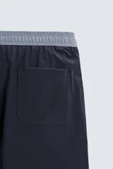 Bañador de hombre azul marino con cintura elástica gris y cordón ajustable. Presenta un pequeño texto estampado en relieve en la parte inferior izquierda.