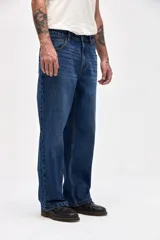 Jean de corte holgado en cadera, cintura y piernas, con diseño clásico de cinco bolsillos y cierre frontal con botón y cremallera.