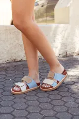 Sandalias bajas color celeste y beige, con base marrón y tiras de cuero con ajuste de velcro.