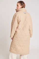 Campera larga acolchada color beige, con diseño de costuras onduladas, cuello alto, cierre frontal con botones a presión y bolsillos laterales amplios.