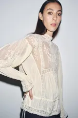 Blusa color crema de algodón con cuello alto, manga larga y bordados florales.