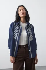 Camisa de manga larga en color azul oscuro con bordados florales en hilo blanco a lo largo de la botonadura frontal. Presenta cuello clásico y corte relajado.