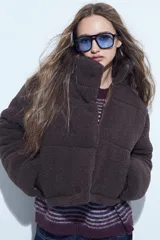 Campera puffer de corderito negro con cuello alto y diseño oversized. Presenta una textura tipo teddy, cierre frontal y corte a la cintura.