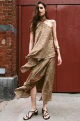Falda midi de tiro alto y diseño asimétrico con cierre frontal cruzado y botón decorativo. Presenta una textura rústica con estampado sutil y forro interior marrón.